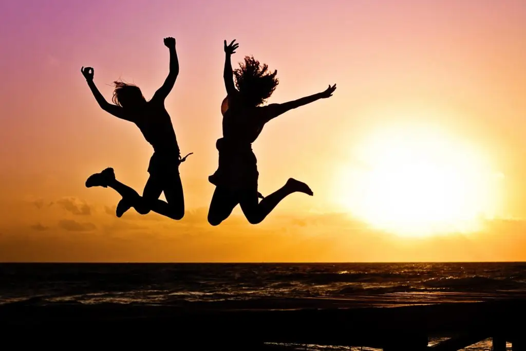 Two people joyfully jumping in silhouette against a vibrant sunset over the ocean.