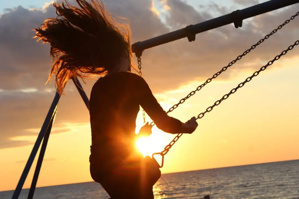 Silhouette of a woman with flowing hair on a swing against a golden sunset over the ocean.